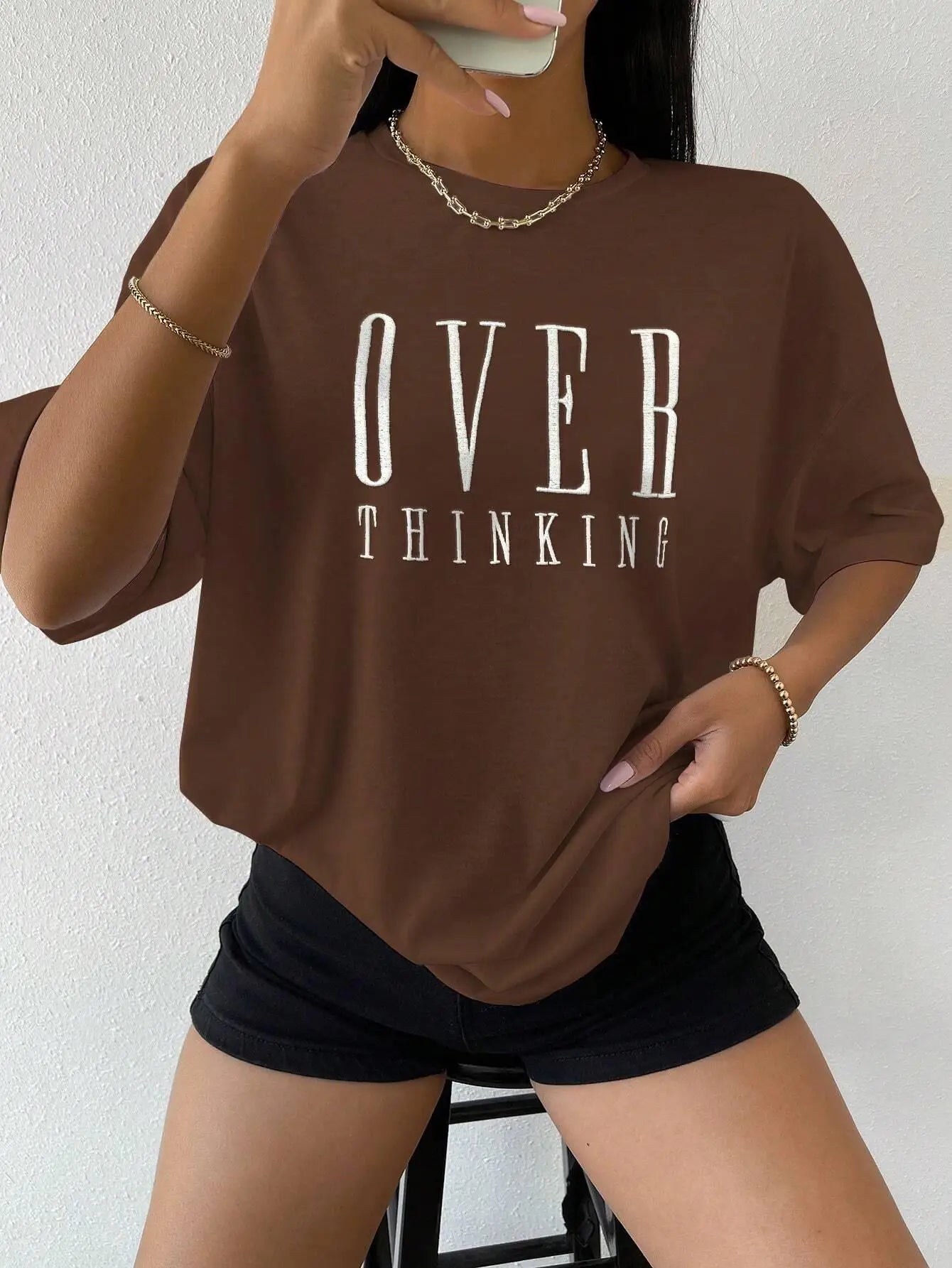 Person wearing a brown 'OVER THINKING' t-shirt against a white background