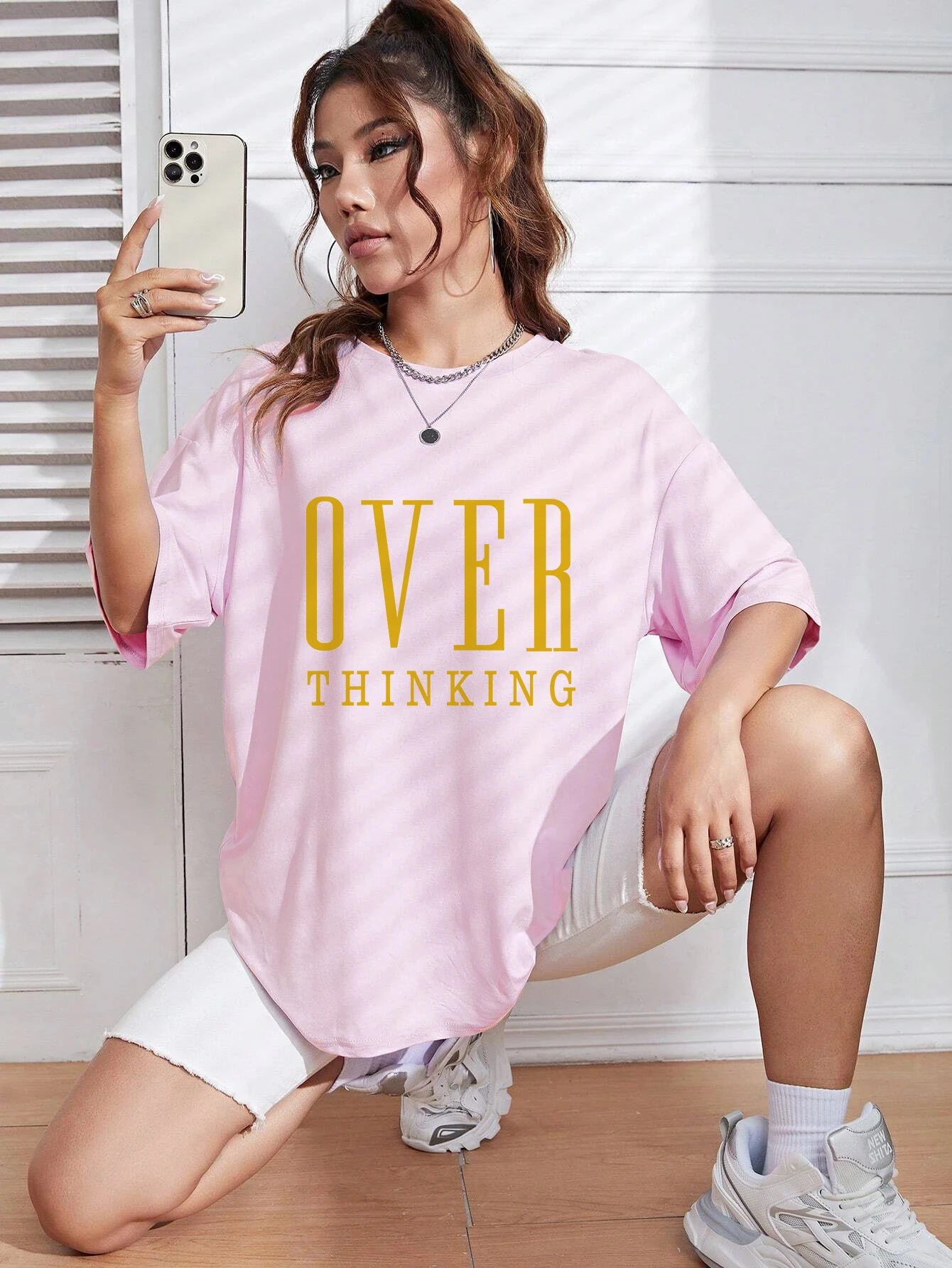 Person wearing a pink t-shirt with 'OVER THINKING' text, taking a selfie indoors.