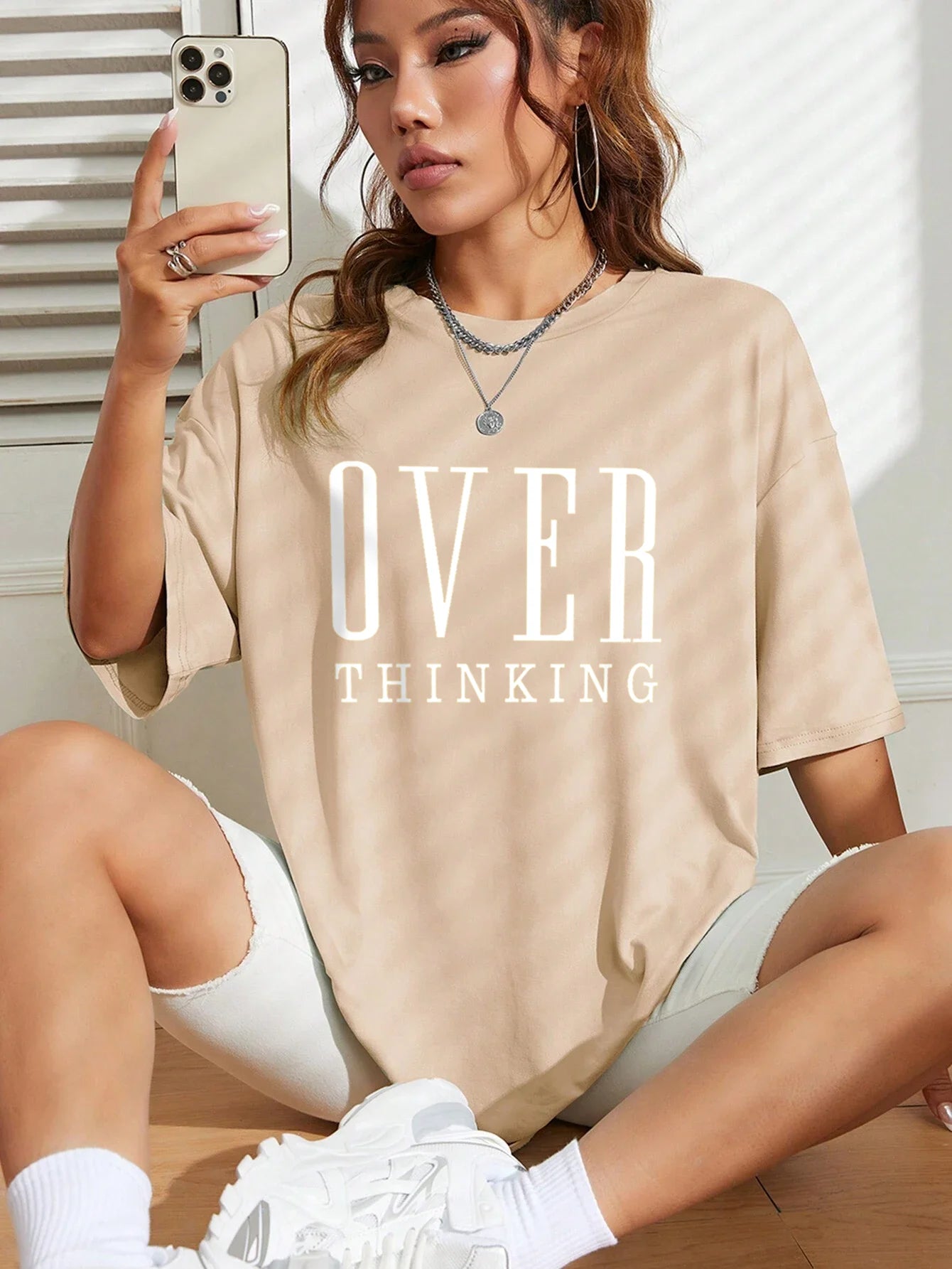Person wearing a beige t-shirt with 'OVER THINKING' text, sitting on the floor.