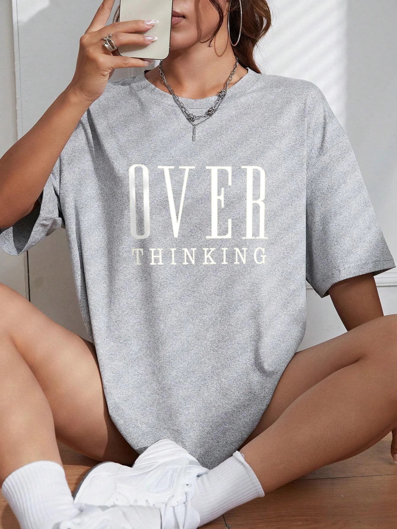 Person wearing a gray t-shirt with 'OVER THINKING' text, sitting indoors.
