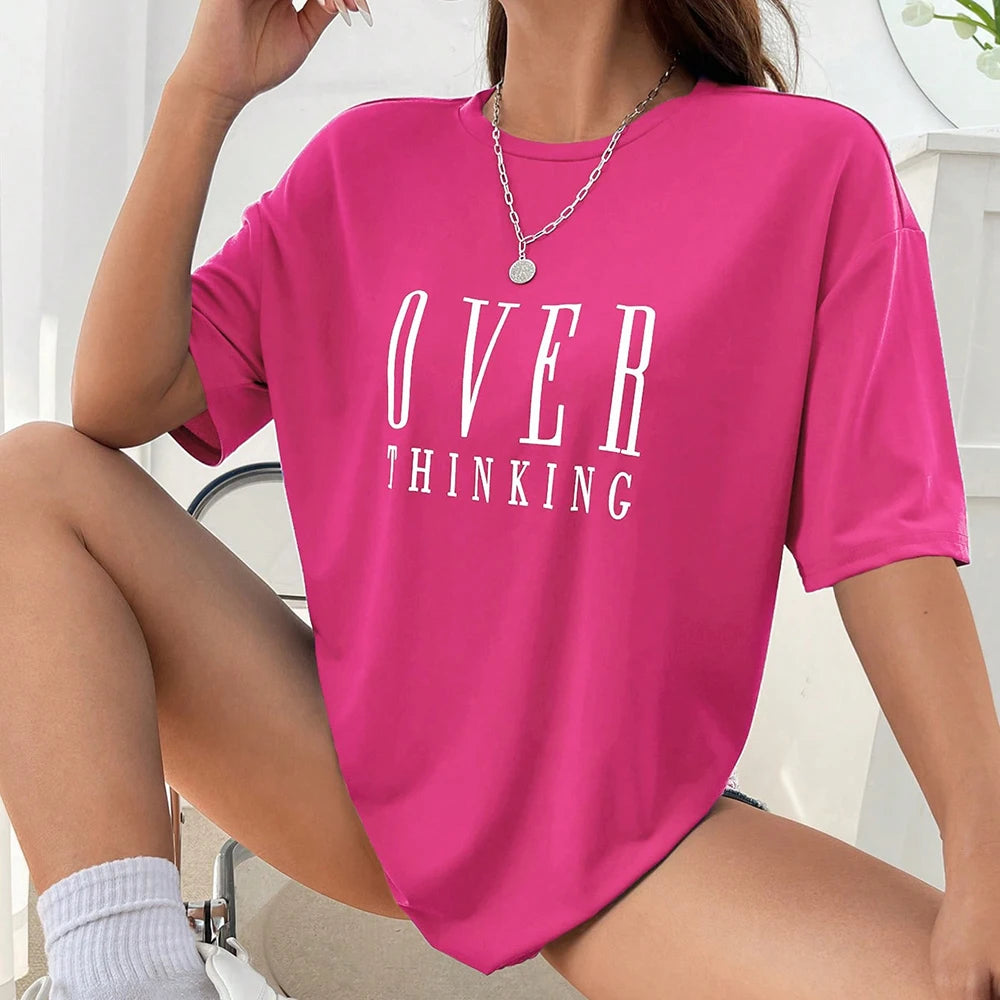 Person wearing a pink t-shirt with 'OVER THINKING' text, sitting indoors.