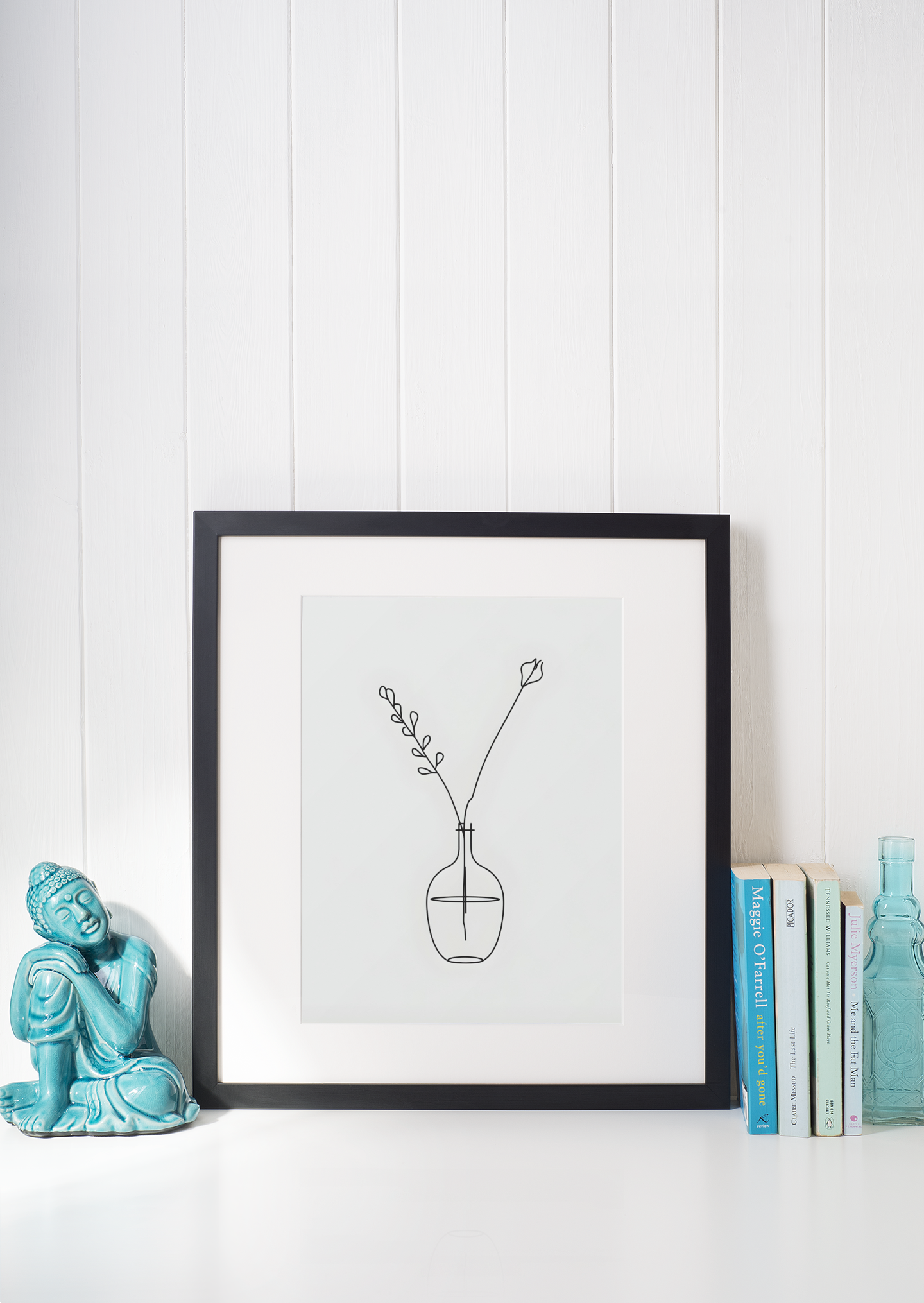 Framed artwork of a minimalistic plant design on a white surface with decorative items.