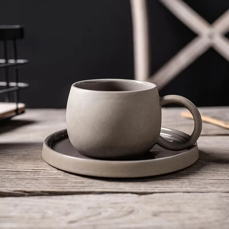 Gray ceramic mug with handle on a matching coaster on a wooden surface.