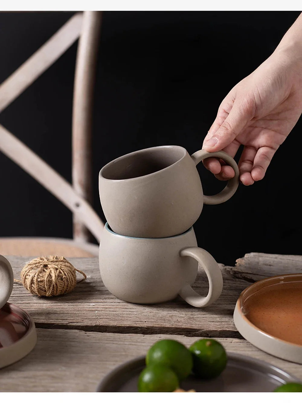 Person holding a stack of ceramic mugs on a wooden surface with a dark background