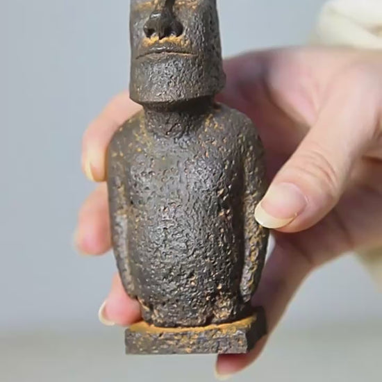 Video of aLarge Moai-inspired resin ornament with a distressed stone-effect finish displayed on a wooden surface.