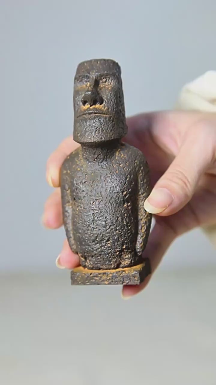 Video of aLarge Moai-inspired resin ornament with a distressed stone-effect finish displayed on a wooden surface.