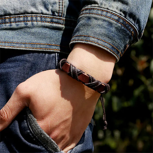 Close-up of a hand wearing a braided leather bracelet with a blurred natural background