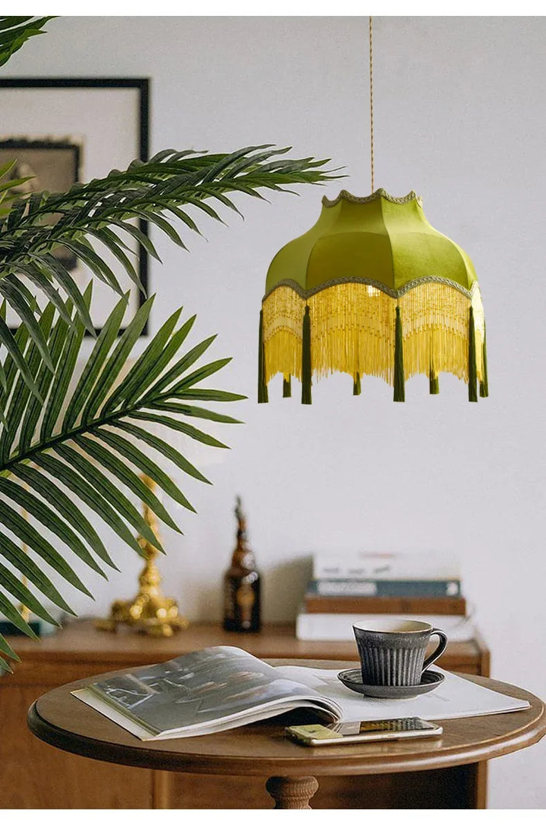 Green pendant lamp hanging above a table with a cup and books in a room with a plant.