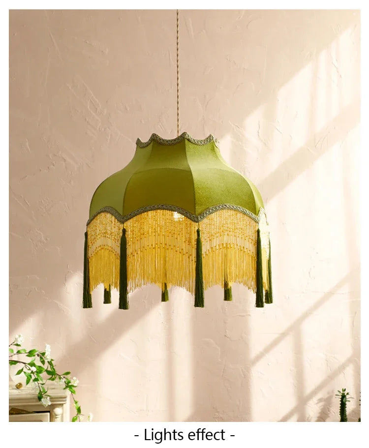 Green lampshade with fringe details hanging against a light wall.