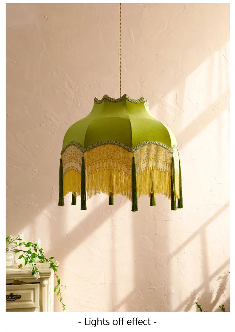Green lampshade with fringe details on a plain wall.