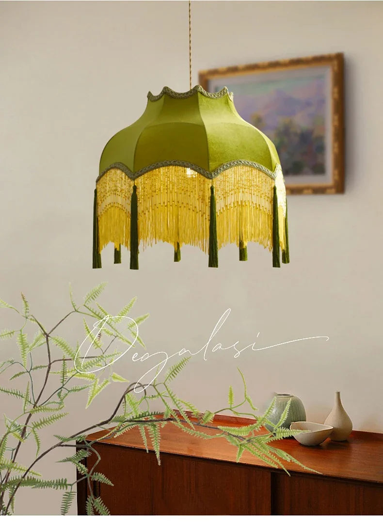 Green lampshade with fringe hanging above a wooden table with decorative items.