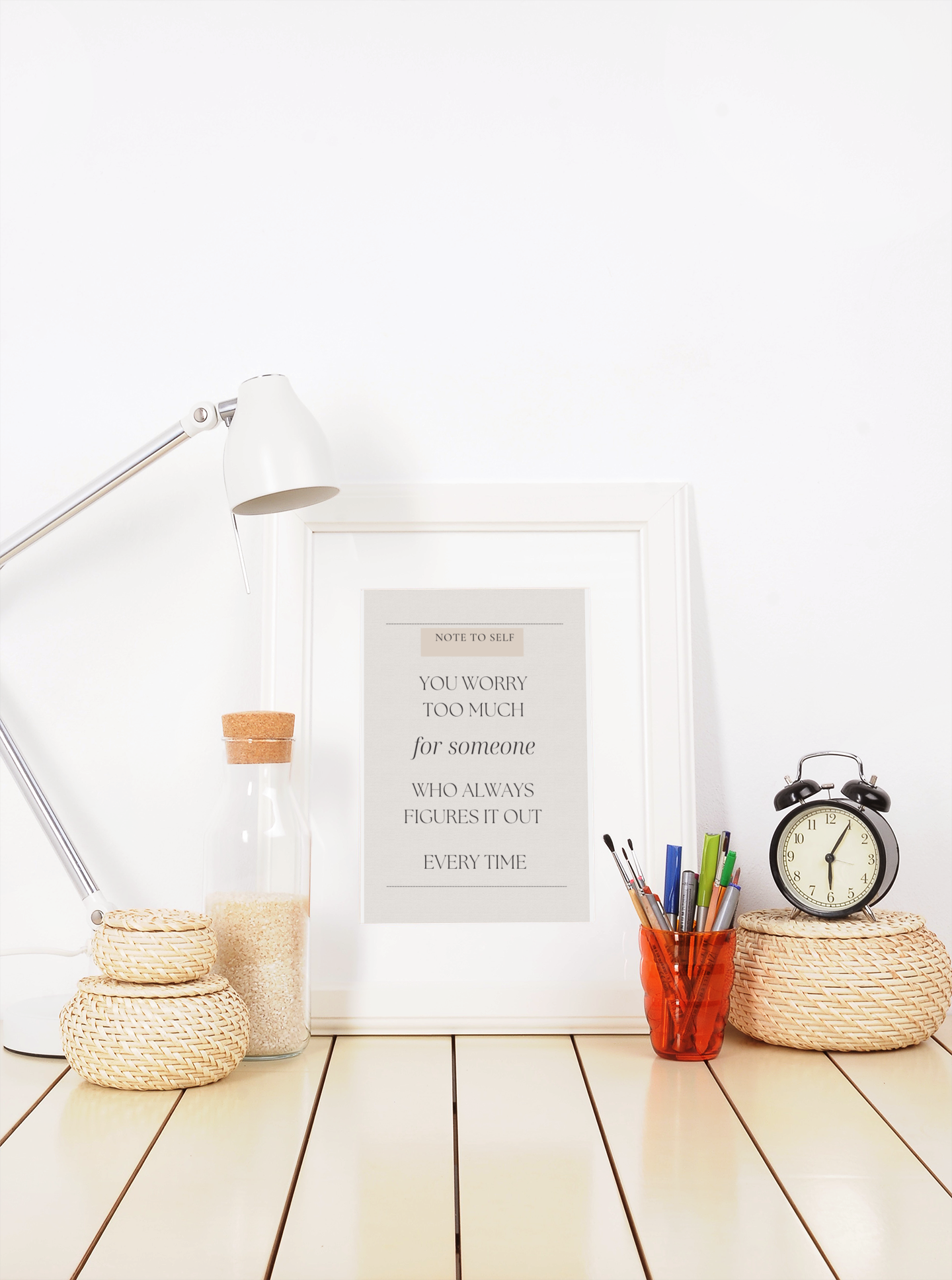 Decorative items including a lamp, framed quote, alarm clock, and stationery on a wooden surface.