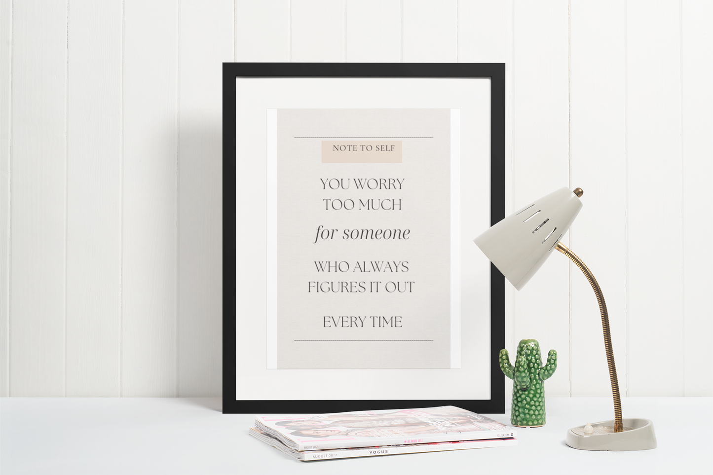 Framed motivational quote on a white wall with a lamp and cactus