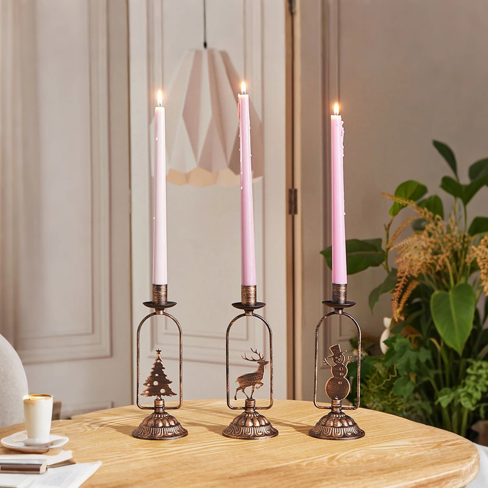 Three decorative candle holders with lit pink candles on a wooden table.