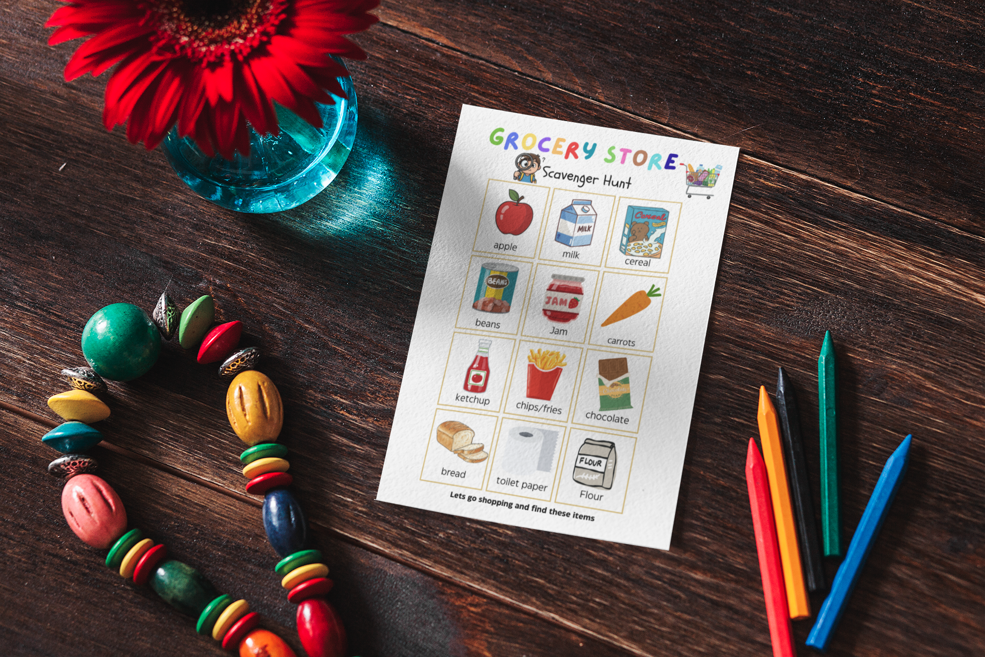 Colorful beaded necklace, grocery store scavenger hunt sheet, and markers on a wooden surface with a red flower.