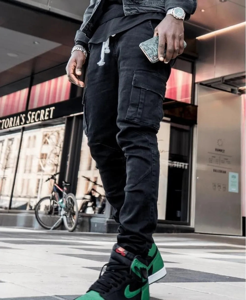 Person wearing black cargo pants and green sneakers in an urban setting with a store in the background.