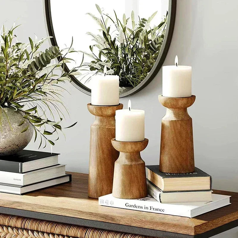 Decorative setup with wooden candle holders, candles, books, and a mirror on a shelf.