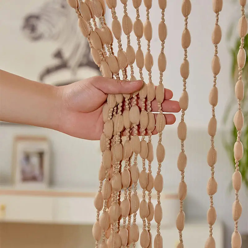 Hand holding a beige beaded curtain with a blurred indoor background