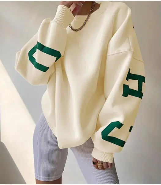Cream-colored sweater with green lettering worn by a person on a neutral background