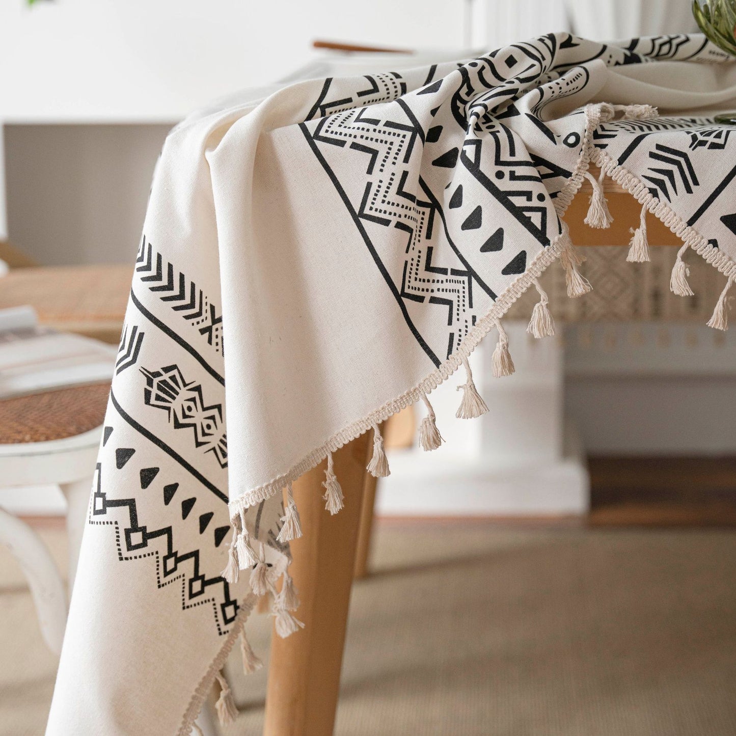 Beige towel with black geometric patterns and tassels draped over a chair.