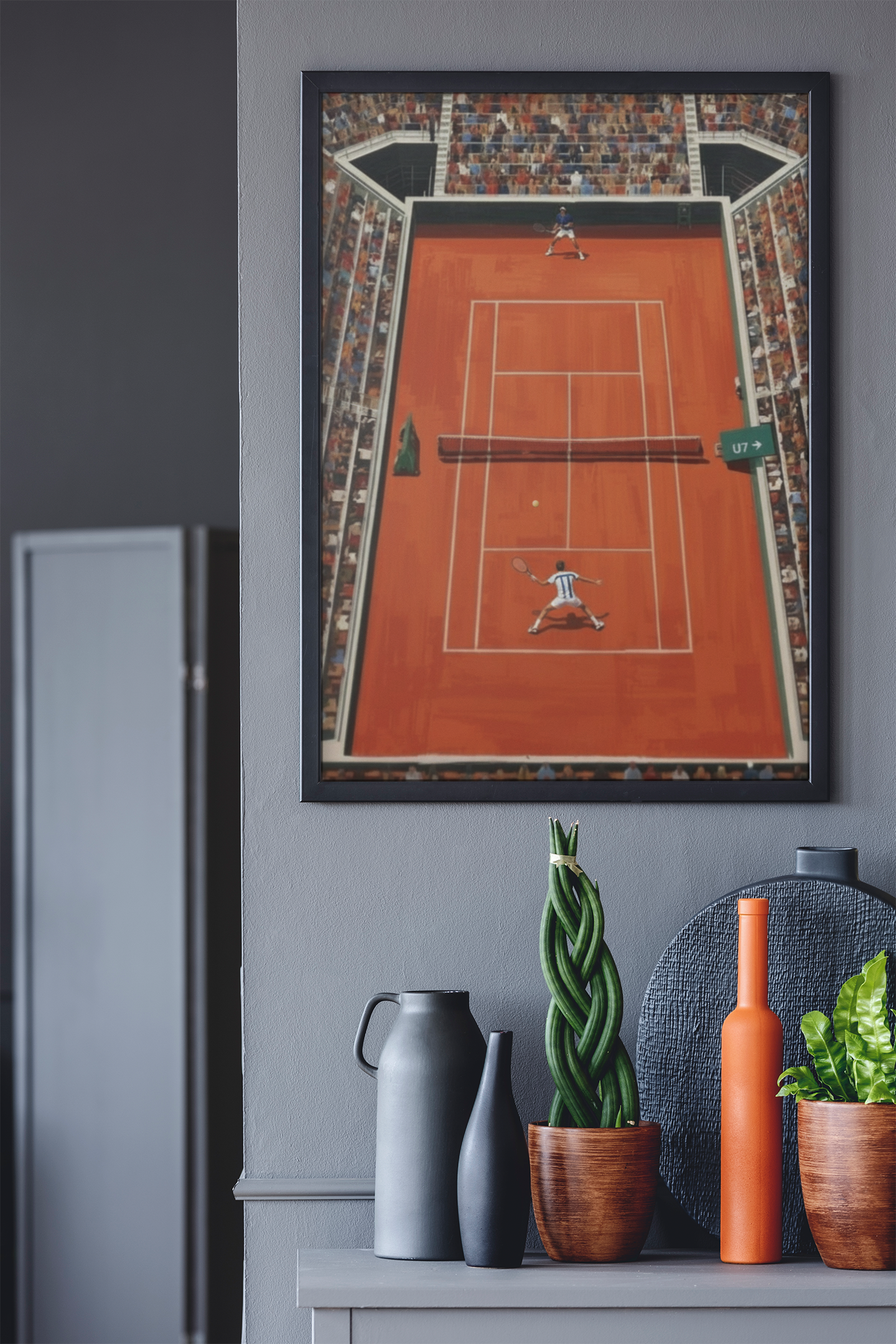 Framed artwork of a tennis court on a gray wall above a shelf with decorative items.