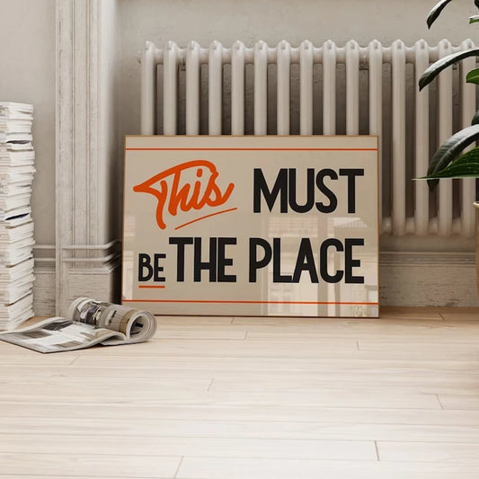 Retro typography poster reading “This Must Be The Place” in black and orange on canvas.
