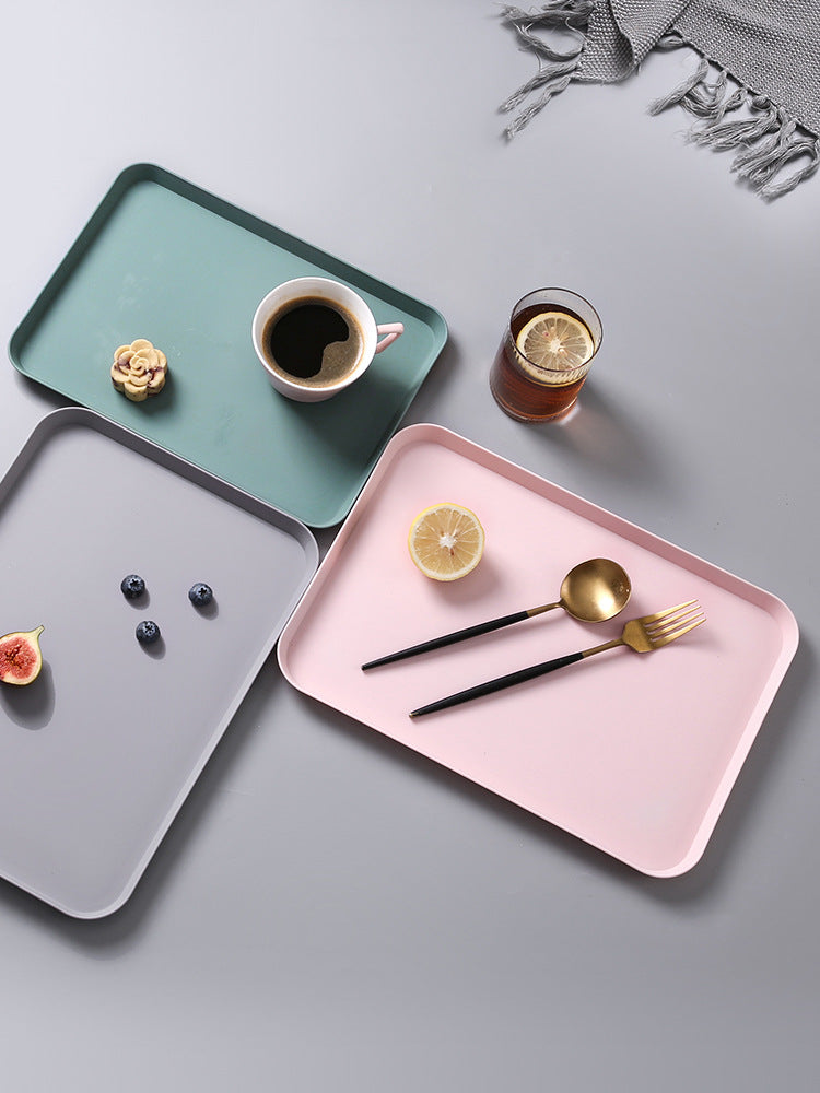 Three trays in green, pink, and gray with food and drink on a light gray background