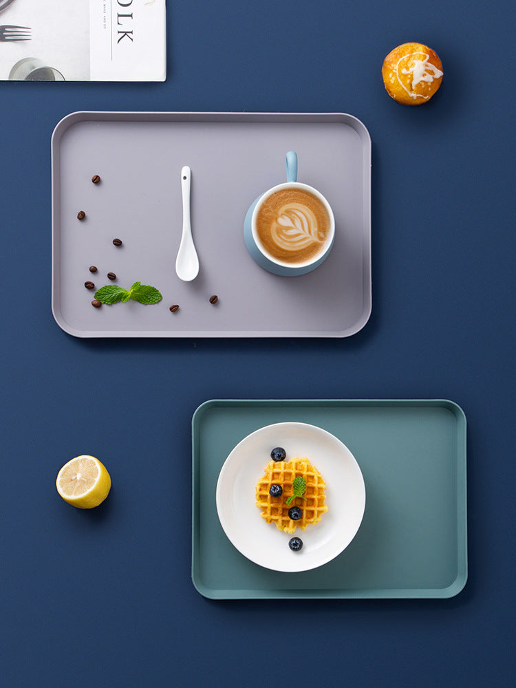 Two trays with a cup of coffee, waffle, lemon, and other items on a blue background