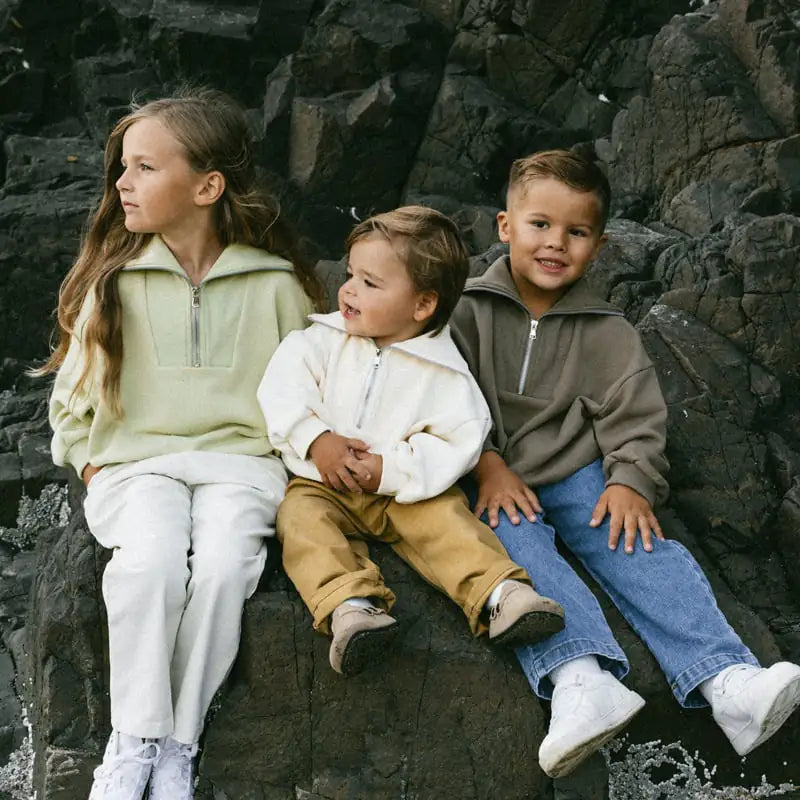 Three children sitting on a rocky surface wearing matching outfits.