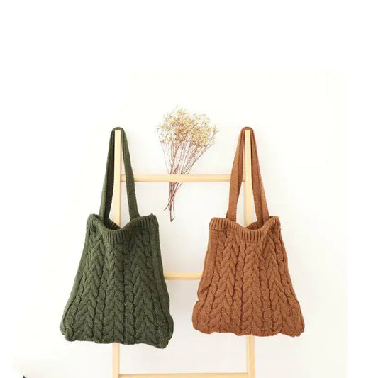 Green and brown plush knit shoulder bags hanging side by side on a wooden rack with dried flowers on a white wall background