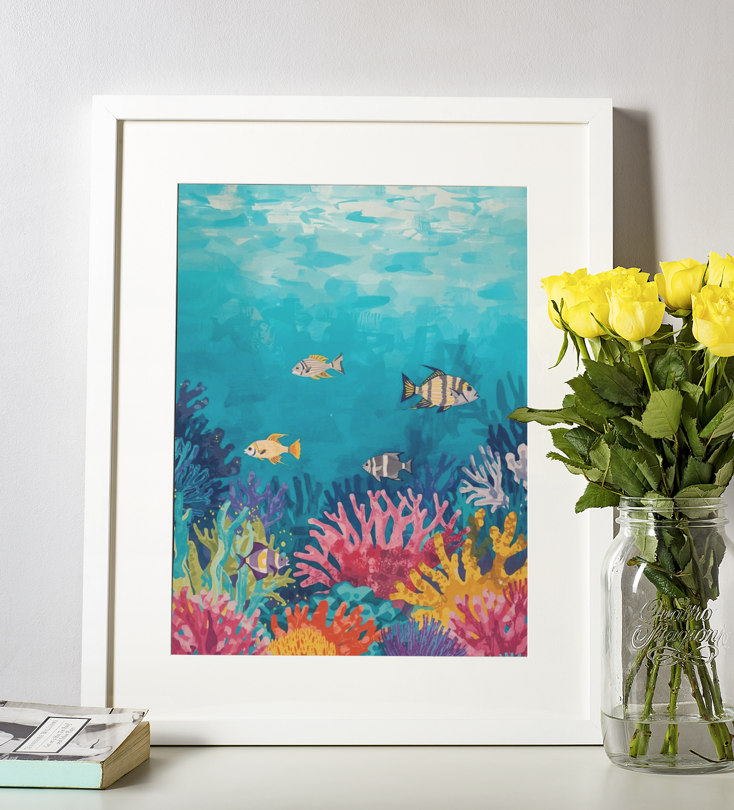 Framed artwork of an underwater scene with fish and coral next to a vase of yellow roses.