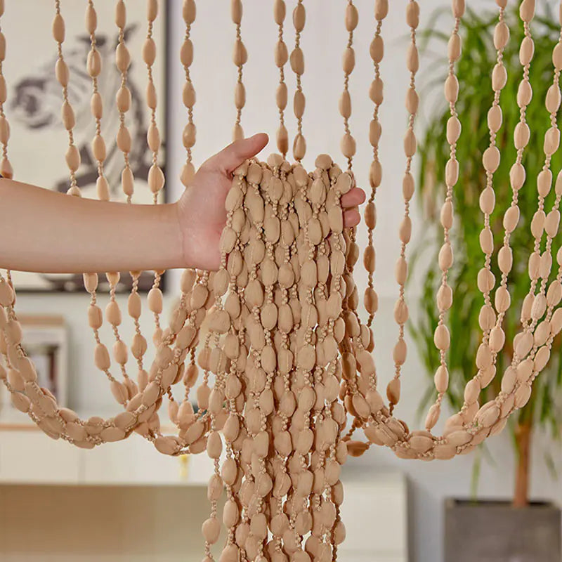 Hand holding a beige beaded curtain with a blurred indoor background