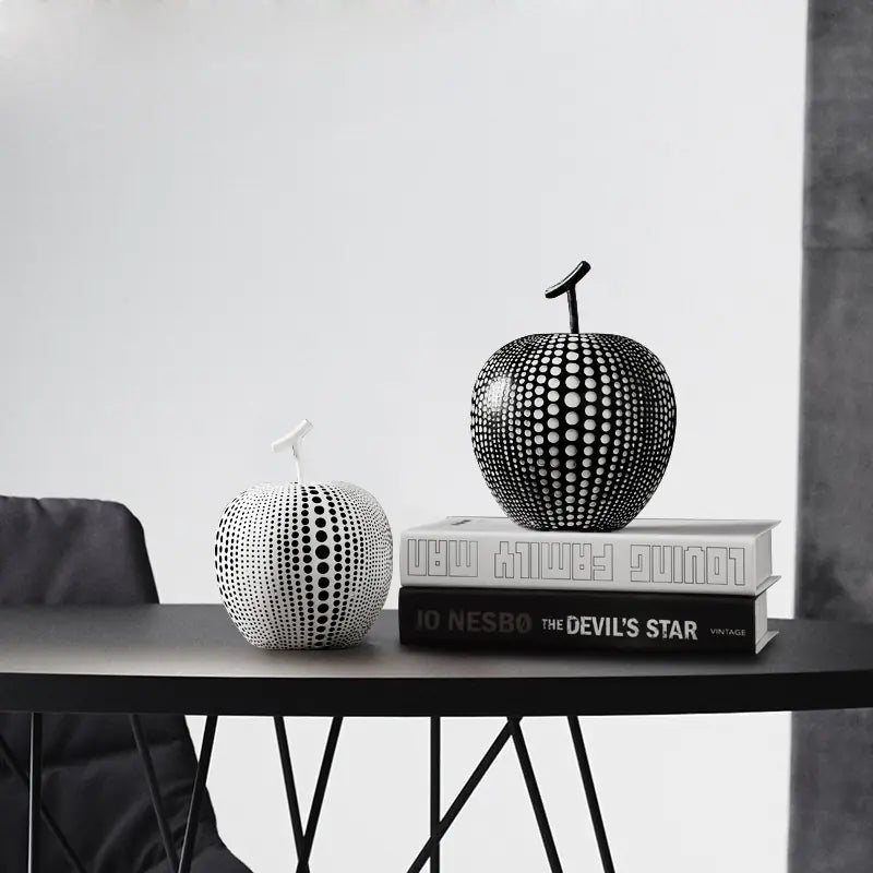 Black and white decorative apple-shaped objects on a table with books underneath.