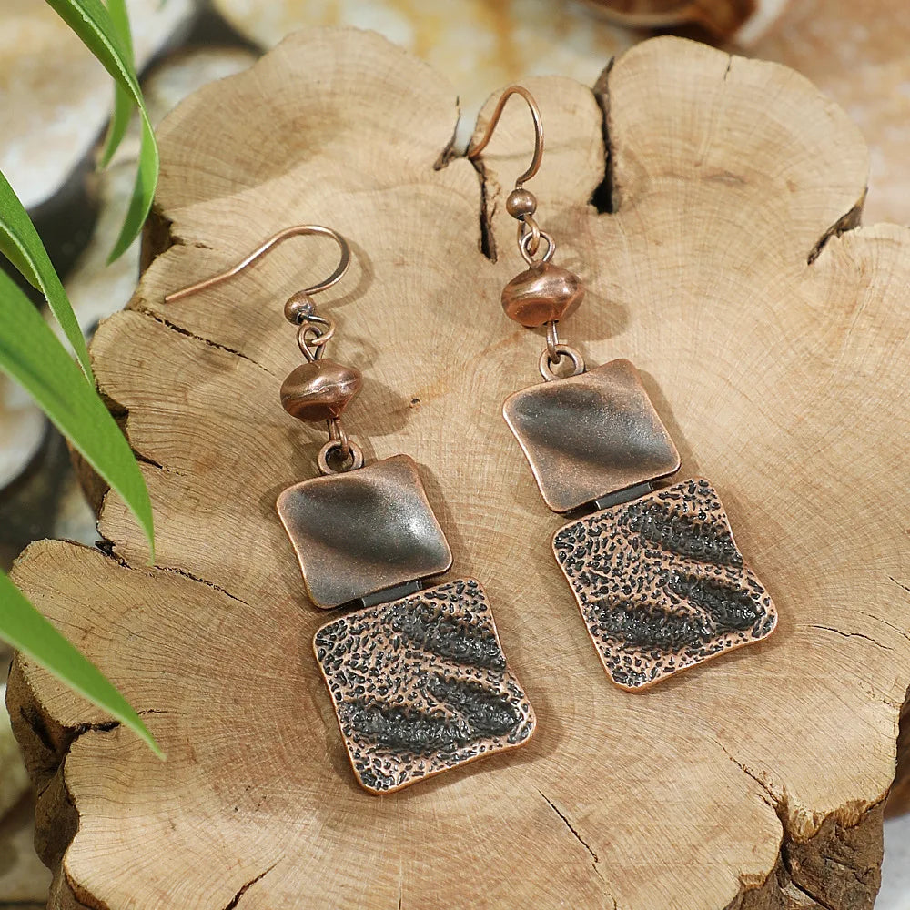 Pair of bronze earrings on a wooden surface with a natural background