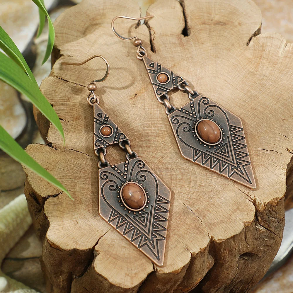 Pair of bronze-colored earrings with brown gemstones on a wooden surface.