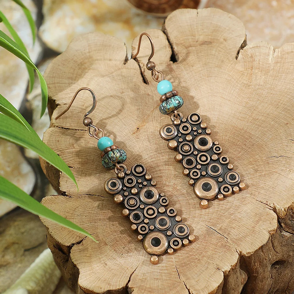 Pair of earrings with circular patterns and turquoise beads on a wooden surface.