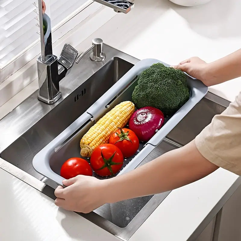 Person using a kitchen sink with a built-in vegetable holder containing vegetables.