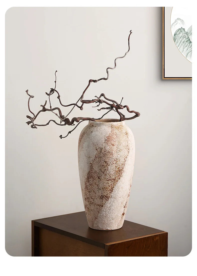 Decorative vase with textured surface and branches on a wooden stand against a light wall.