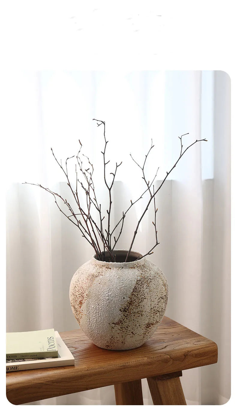 Decorative vase with branches on a wooden table against a white curtain background