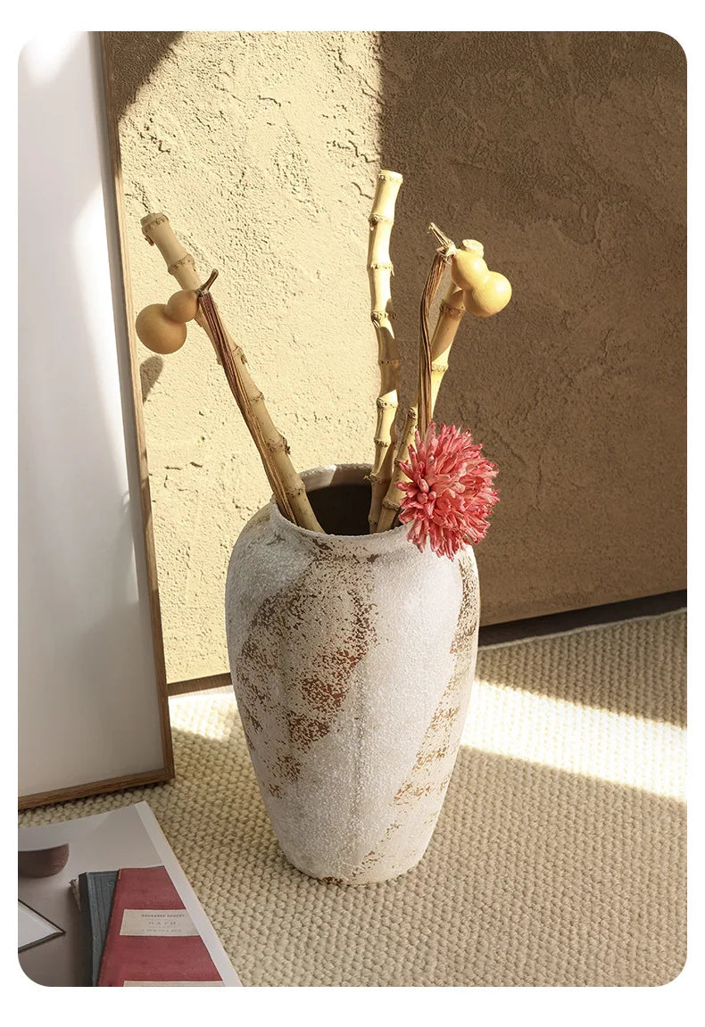 Decorative vase with dried branches and a pink flower on a textured surface