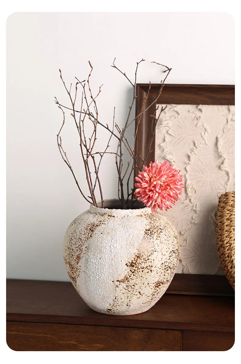 Decorative vase with pink flower and branches on a wooden surface