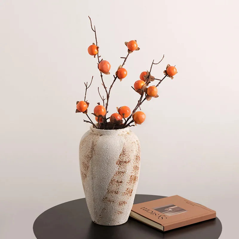 Decorative vase with orange branches on a table against a plain background