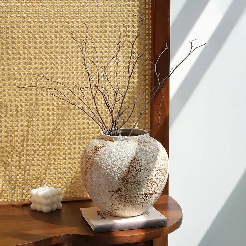 Decorative vase with branches on a wooden surface against a textured wall.