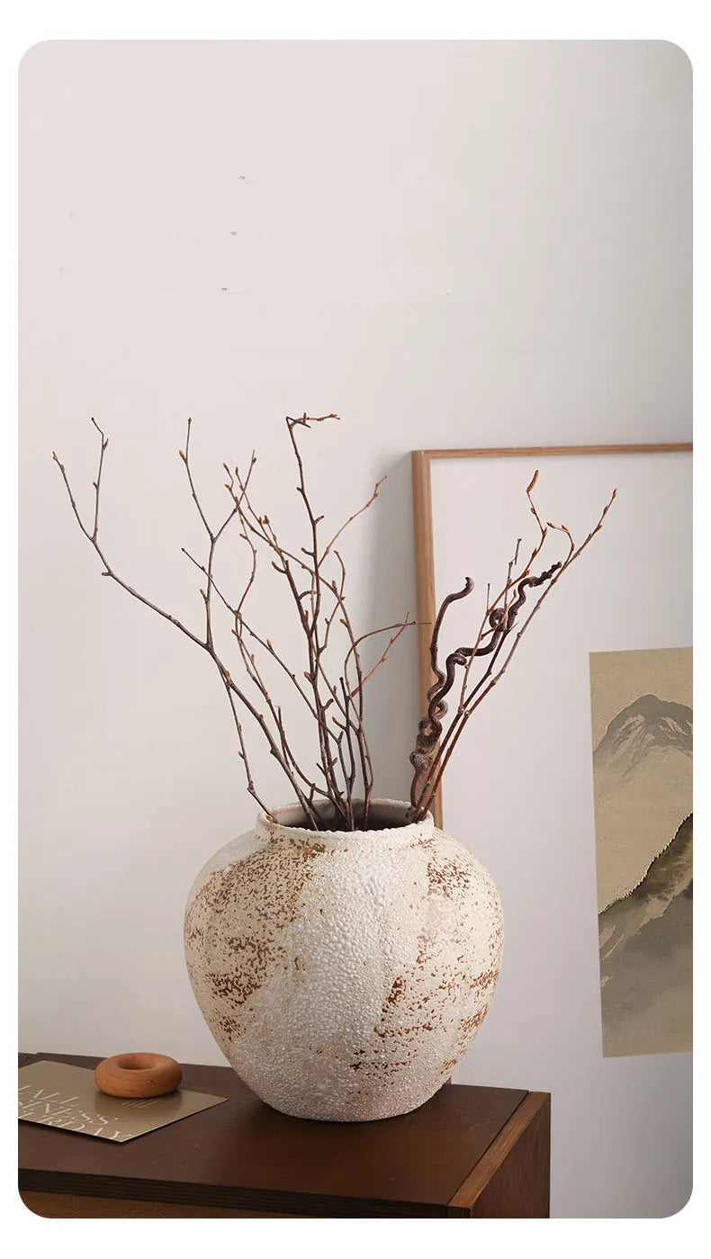 Decorative vase with branches on a wooden surface against a light wall.
