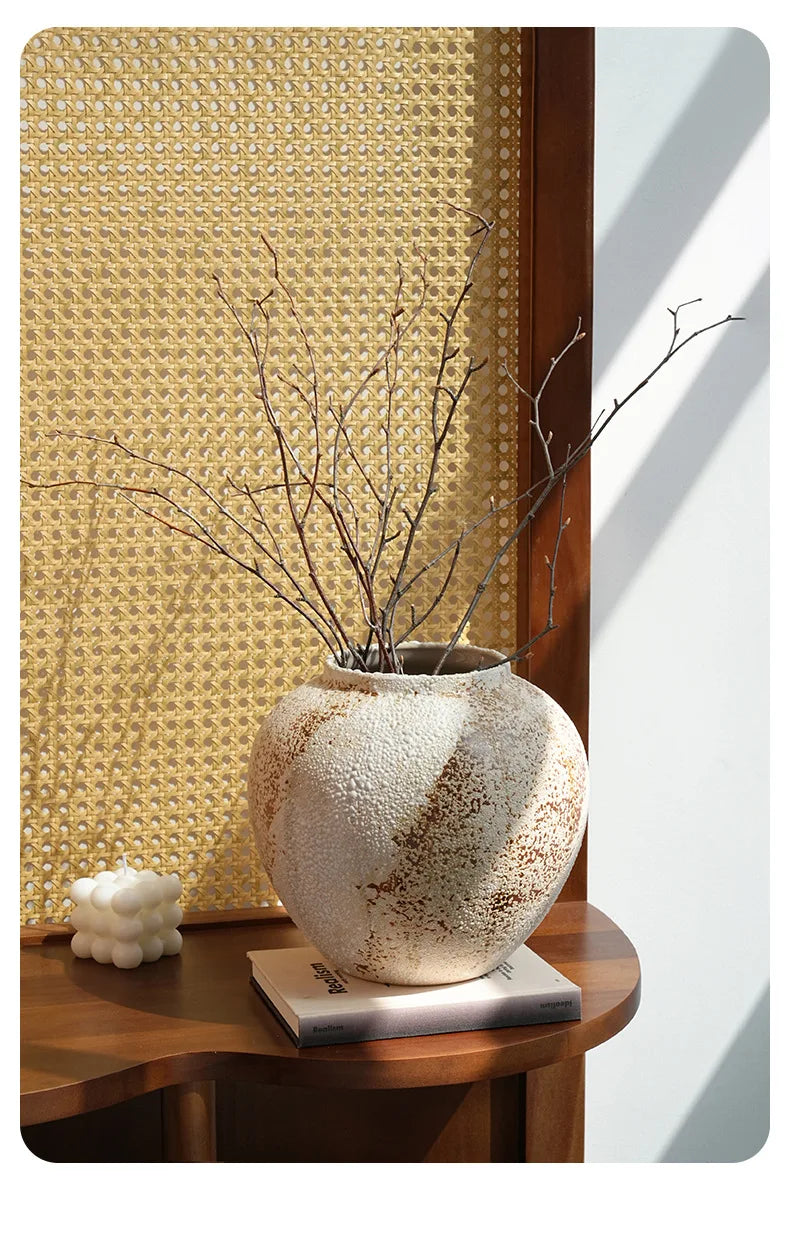 Decorative vase with branches on a wooden table against a textured wall.