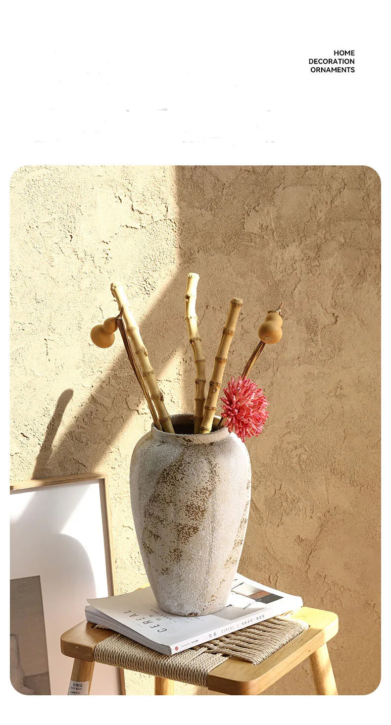 Decorative vase with branches and a pink flower on a wooden stool against a textured wall.