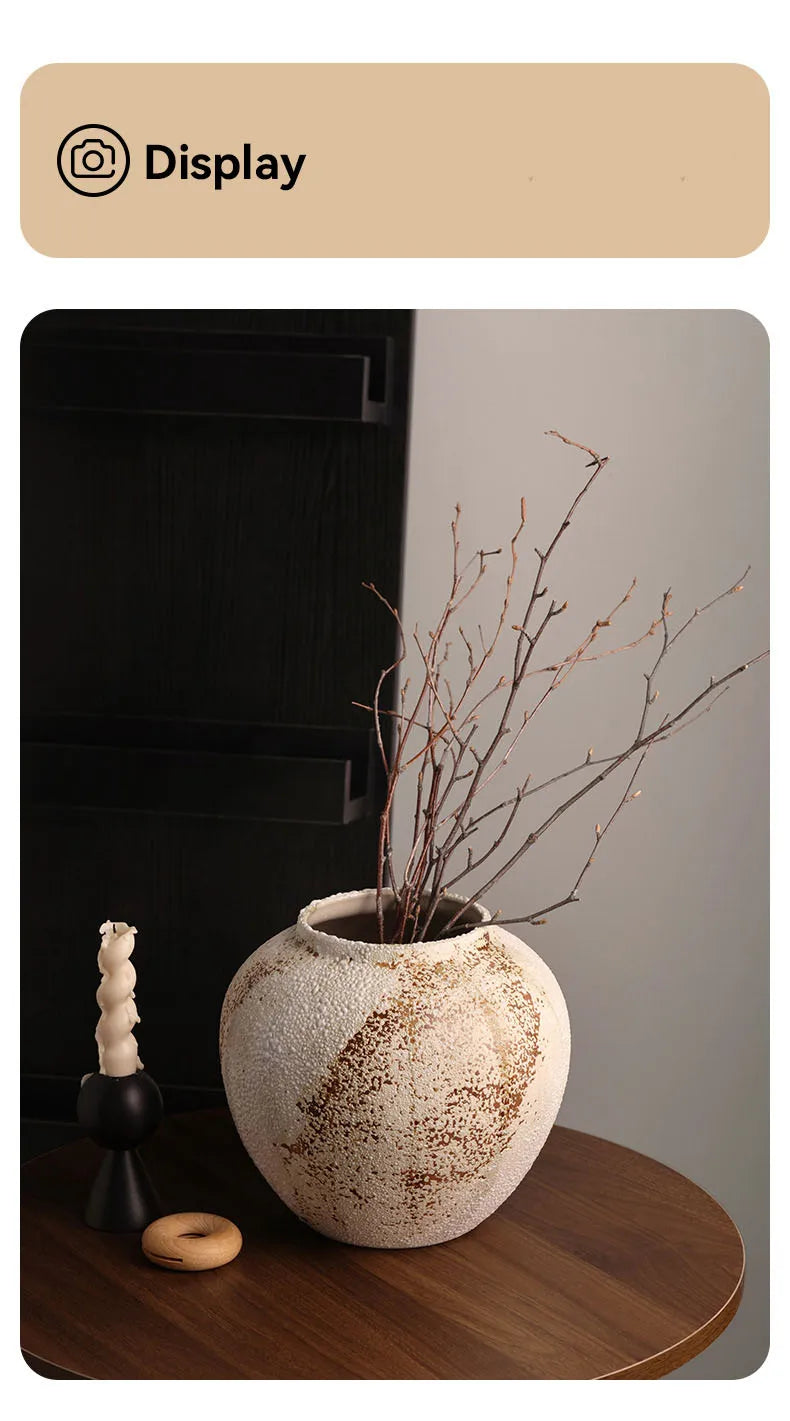Ceramic vase with branches on a wooden surface, with a black appliance in the background.
