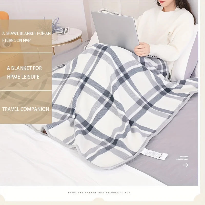 Person using a laptop under a plaid blanket in a cozy room setting