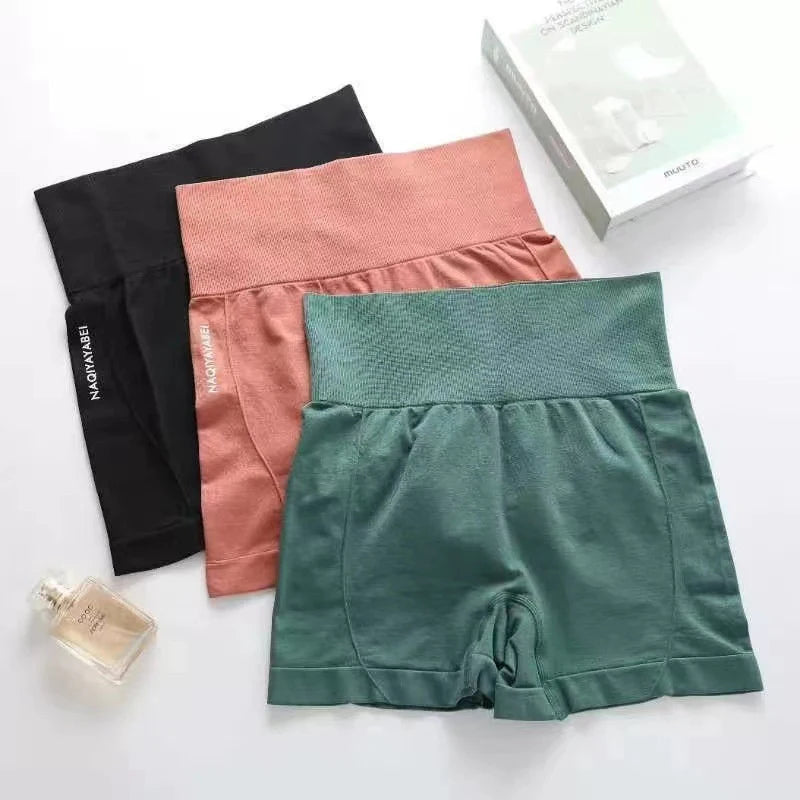 Three pairs of women's active shorts in black, pink, and green on a white surface with a perfume bottle.