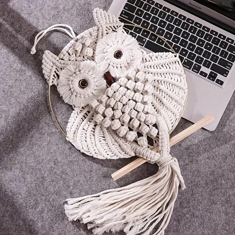 Macrame owl wall hanging on a gray surface next to a laptop.
